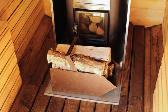 Wooden sauna interior with traditional stove. Burning firewood in metal heater. Rustic wellness atmosphere with warm wooden walls and floor. Natural relaxation place for health spa therapy.
