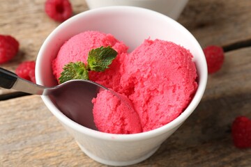 Taking delicious raspberry sorbet with mint from bowl with spoon at wooden table, closeup