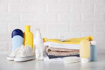 Different baby clothes and accessories on table near brick wall