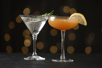 Different martini cocktails in glasses on black table against blurred lights, closeup