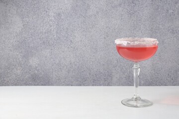 Martini cocktail with sugar in glass on white table near grey wall. Space for text
