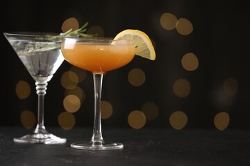 Different martini cocktails in glasses on black table against blurred lights, closeup. Space for text