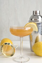 Martini cocktail with lemon slice in glass, fruits and shaker on white wooden table, closeup