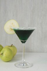 Martini cocktail with apple slice in glass and fruits on white table, closeup