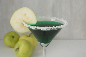 Martini cocktail with apple slice in glass and fruits on white table, closeup