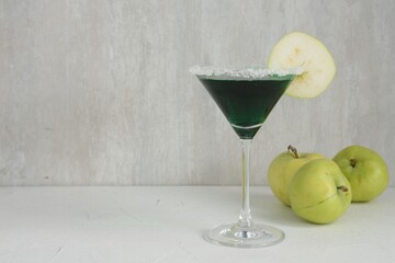 Martini cocktail with apple slice in glass and fruits on white table, closeup. Space for text