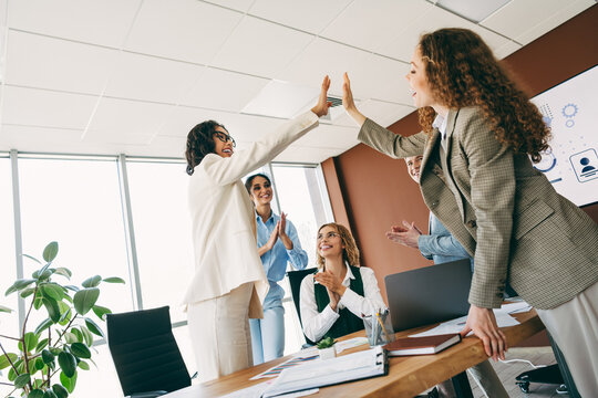 Professional team celebrating success with a high five in a contemporary office setting, promoting teamwork and collaboration