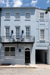 Charleston, South Carolina, USA - July 2, 2025. Elegant pastel blue rowhouse with wrought iron balcony and black door.