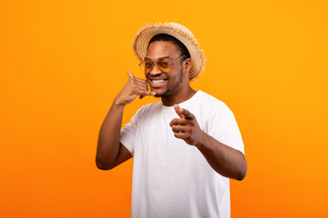 Flirty African American guy in trendy summertime outfit showing CALL ME gesture, smiling at camera...