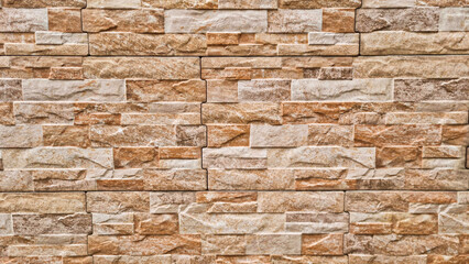 Pattern of rectangular beige and brown stone tiles with layered rough surface forming a decorative wall cladding. Natural construction material photography. 