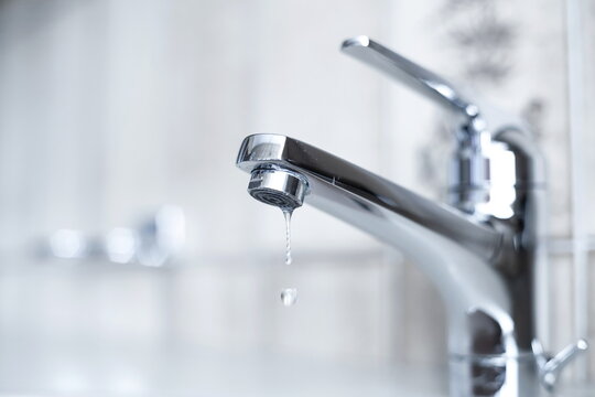Dripping tap with water droplets inside apartment bathroom. Macro, close up shot, shallow depth of field, no people