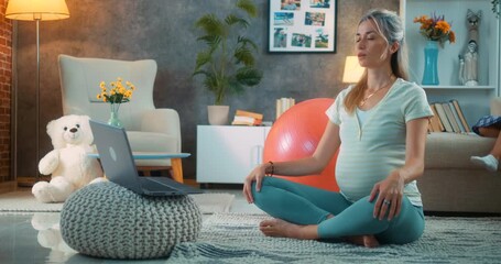 Pregnant woman sitting in lotus position on living room floor, starting meditation with laptop playing music or online tutorial, focusing on relaxation while her daughter is jumping around the room. - Powered by Adobe