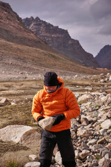 A man carries a stone in his hands in the mountains. A tourist man builds a stone shelter from the wind in the mountains