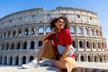 A young woman poses joyfully at the iconic Colosseum in Rome, fully embodying the spirit of adventure and travel, while enjoying the vibrant culture and historic landmarks this city offers
