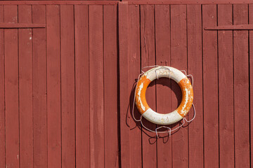 Lifebuoy hanging on wooden wall at seaside location. Classic maritime safety equipment, symbol of rescue, SOS, and nautical protection in coastal environment