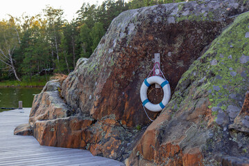 Lifebuoy placed on coastal rocks by the sea. Symbol of safety, rescue, and maritime emergency equipment in natural environment near water
