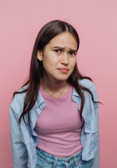 Fototapeta premium Young woman with a puzzled expression against a pink background.