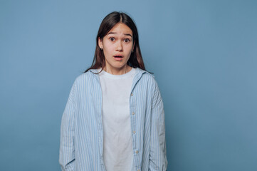A surprised young woman in a striped shirt against a blue background.