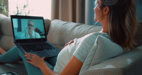 Pregnant woman lying on sofa in living room during online video call consultation with female doctor, focusing on prenatal care, telemedicine, and digital healthcare from home. - Powered by Adobe