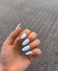 Female hand with long blue manicure nails holding against a stone pavement background. Beauty and style concept.