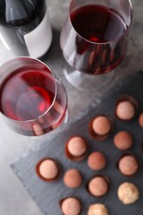 Tasty truffle bonbons and red wine on grey table, flat lay