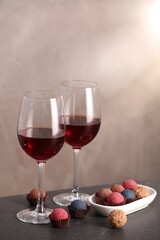 Delicious truffle bonbons and wine on black table against grey background