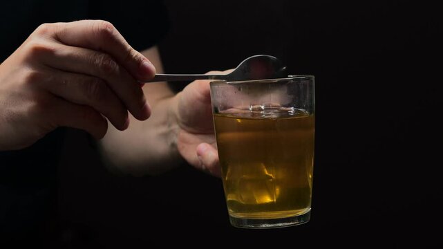 Man stirring sugar in tea with teaspoon on black isolated background.
Hand holding teaspoon in glass.
Hot drink and tea boat inside