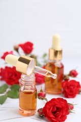 Bottles of essential oil and red roses on white table, closeup