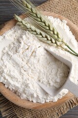 Flour in bowl and green wheat spikes on wooden table, top view