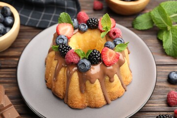 Tasty Bundt cake with berries, chocolate and mint on wooden table, closeup