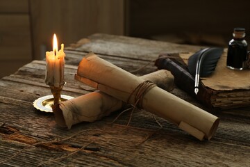 Old paper scrolls, book, feather, inkwell and burning candle on wooden table, closeup