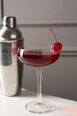 Tasty cherry cocktail and shaker on white table, closeup