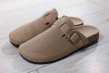 Stylish beige slippers on light wooden floor, closeup