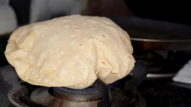 Close up shot of cooking a wheat roti or chappati being roasted puffed and swollen on a blue gas flame in the kitchen.
