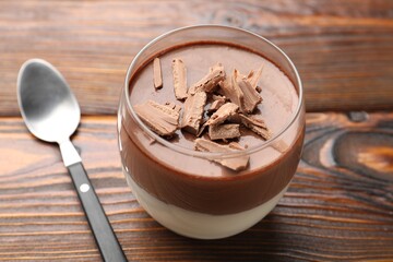 Delicious chocolate panna cotta in glass and spoon on wooden table, closeup