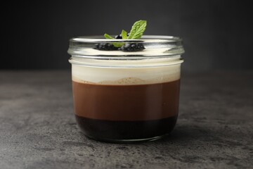Tasty panna cotta with blackberries and mint in jar at grey table, closeup