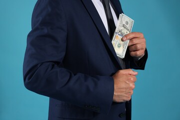Man putting dollars in pocket on blue background, closeup