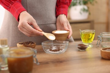Making natural scrub. Woman adding sugar into bowl at wooden table, closeup