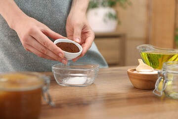 Making natural scrub. Woman adding coffee into bowl at wooden table, closeup