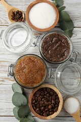 Natural body scrubs in glass jars and ingredients on wooden table, flat lay