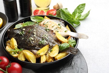 Tasty roasted flounder fish with herbs, potato and tomatoes on light table, closeup. Homemade seafood dish