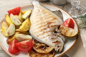 Tasty roasted flounder fish served with potatoes, tomatoes and lemon slices on light wooden table, closeup. Homemade seafood dish