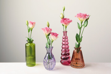Beautiful eustoma flowers in glass vases on white table against light grey background