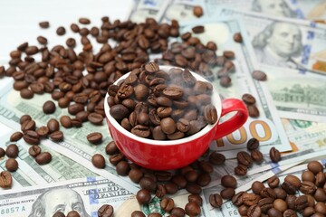 Roasted coffee beans, cup and dollar banknotes on white table, closeup