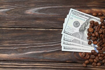 Roasted coffee beans and dollar banknotes on wooden table, flat lay. Space for text