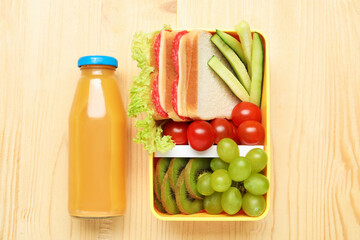 Open lunch box with tasty food and bottle of juice on wooden table, flat lay