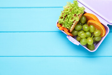 Open lunch box with tasty food on light blue wooden table, top view. Space for text