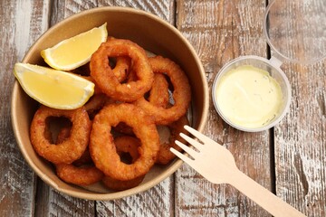 Fried squid rings, lemon and sauce on wooden table, flat lay