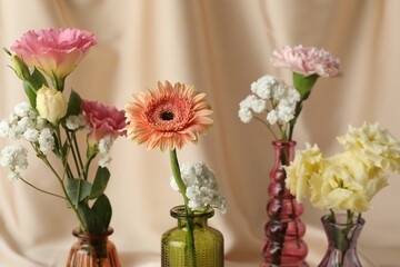 Beautiful flowers in glass vases against beige cloth, closeup