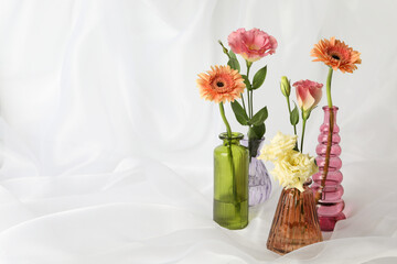 Beautiful flowers in glass vases on white cloth, space for text